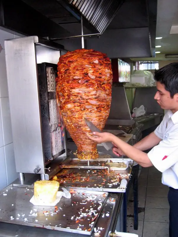 Chef cutting al pastor off of a trompo for tacos